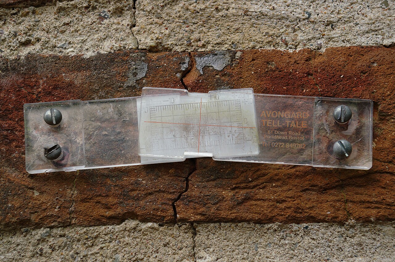 Jauge de fissure fixée en travers d'une fissure de mur en brique Jauge de fissure fixée en travers d'une fissure de mur en brique